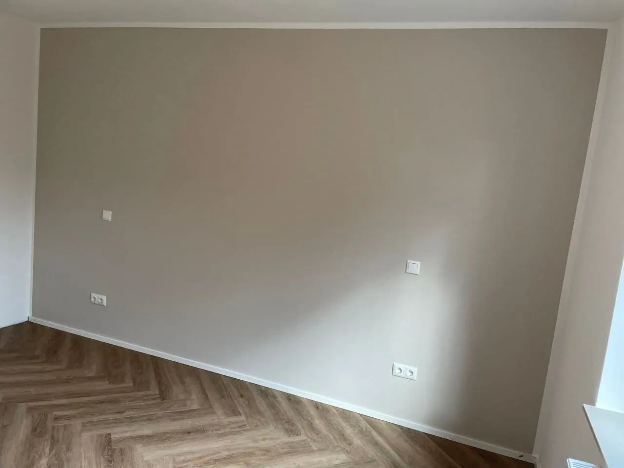 Wohnraum mit frisch gestrichener Wand in warmem Greige und einem Vinylboden im Fischgrätmuster