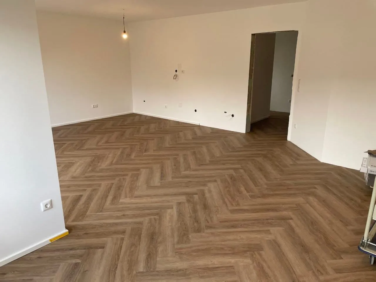 Renovierter Wohnraum mit weißen Wänden und einem Vinylboden im Fischgrätmuster